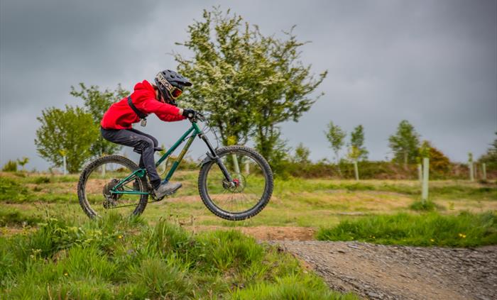 Action shot of a young rider wearing a bright red top against a stormy sky.